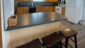 Una cocina moderna con armarios de madera, una isla grande con taburetes, un refrigerador y un ventilador de techo.