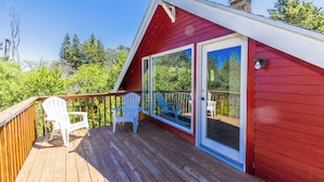 Eine Terrasse mit roten Dachziegeln, zwei weiße Adirondack-Stühle, eine Glastür zu einem weiteren Terrassenbereich und im Hintergrund viel Grün.