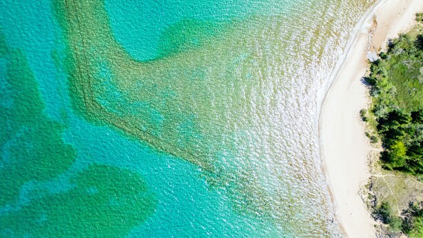 Eine Luftaufnahme eines Strandes mit klarem türkisblauem Wasser und einer Sandküste.