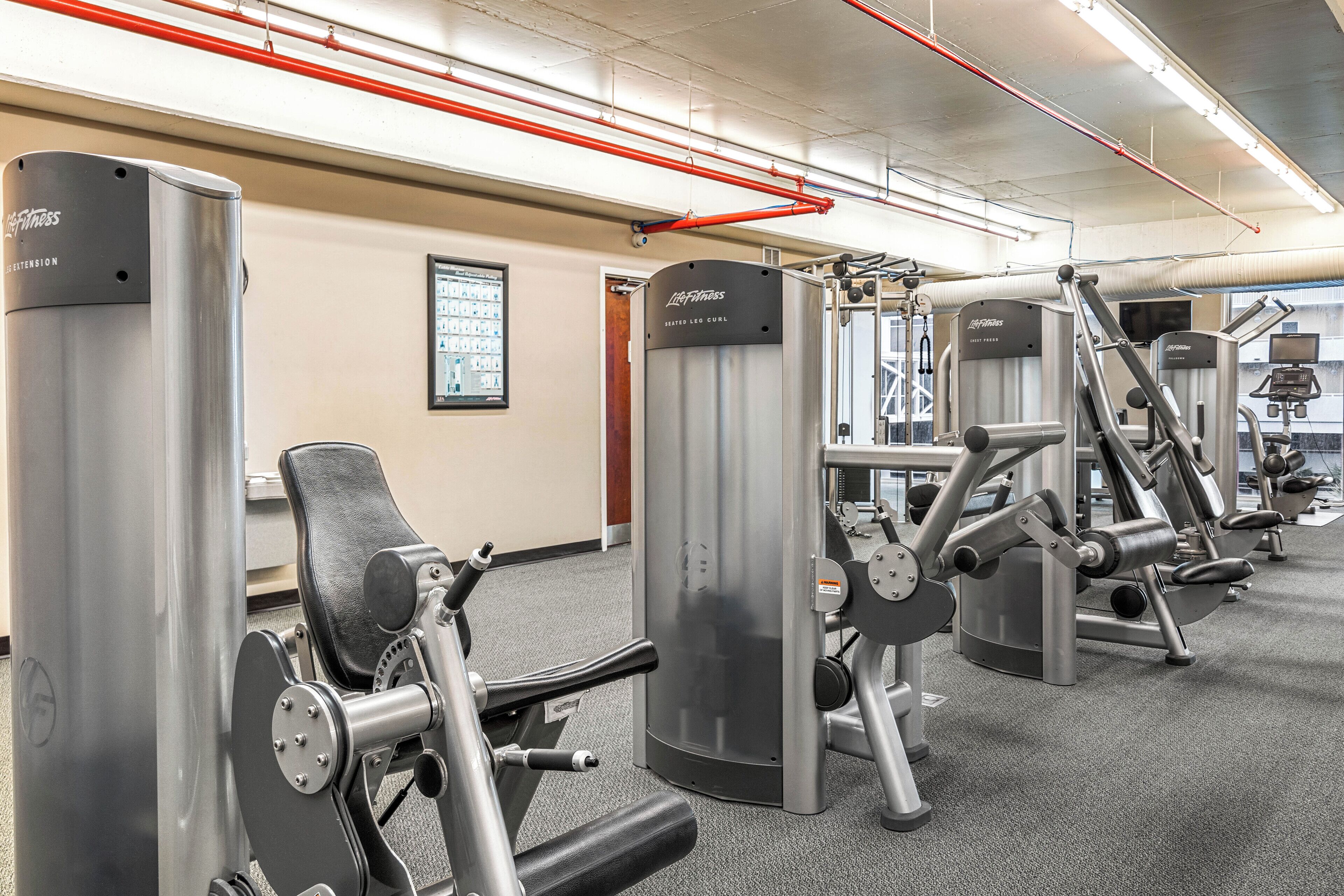Ein Fitnessstudio mit verschiedenen Trainingsgeräten, darunter eine Brustpresse und eine Beinpresse.