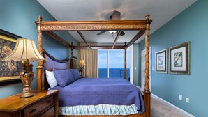 Un letto a baldacchino con vista sull'oceano, un comodino in legno e una ventola a soffitto.