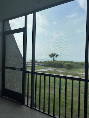 A room with large windows, a balcony with a metal railing, and a view of a grassy area with trees.