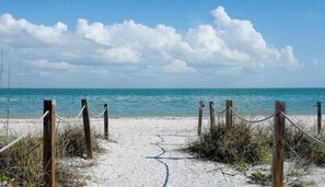 Une plage de sable avec des poteaux en bois et des cordes, qui mènent à l’océan.