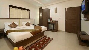 A hotel room with a large bed, a TV, a wardrobe, and a small desk with a chair. - Hotel Mani Ram Palace (Agra)