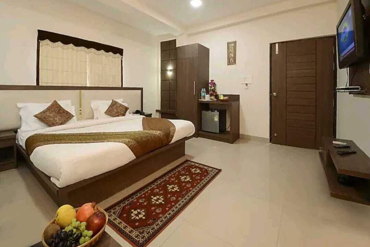 A hotel room with a large bed, a TV, a wardrobe, and a small desk with a chair.