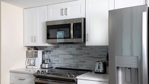 A modern kitchen with stainless steel appliances, including a microwave, oven, and refrigerator, with a tiled backsplash and white cabinetry. - Seaside Serenity-2BD 2BA condo w/ pool, parking, tennis courts, near beaches (Key West)