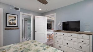 A bedroom with a bed, a dresser, a television, and a door leading to a bathroom. - Seaside Serenity-2BD 2BA condo w/ pool, parking, tennis courts, near beaches (Key West)