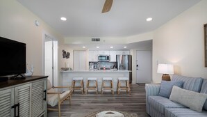 A modern living room with a sofa, a television, and a kitchen in the background. - Seaside Serenity-2BD 2BA condo w/ pool, parking, tennis courts, near beaches (Key West)