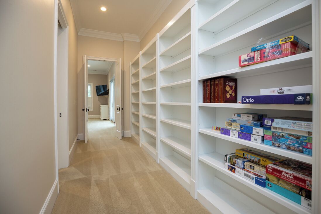 A hallway with a carpeted floor leading to a room with a TV mounted on the wall.