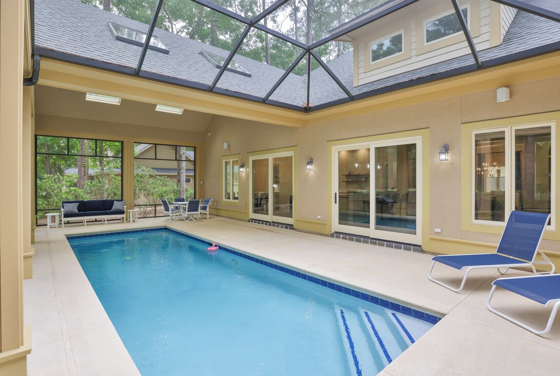 Una piscina interna con pareti in vetro trasparente, piastrelle azzurre e un soffitto con lucernari.