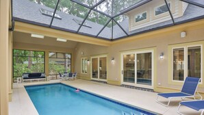 Une piscine intérieure avec des parois en verre transparent, des carreaux de piscine bleus et un plafond doté de lucarnes.