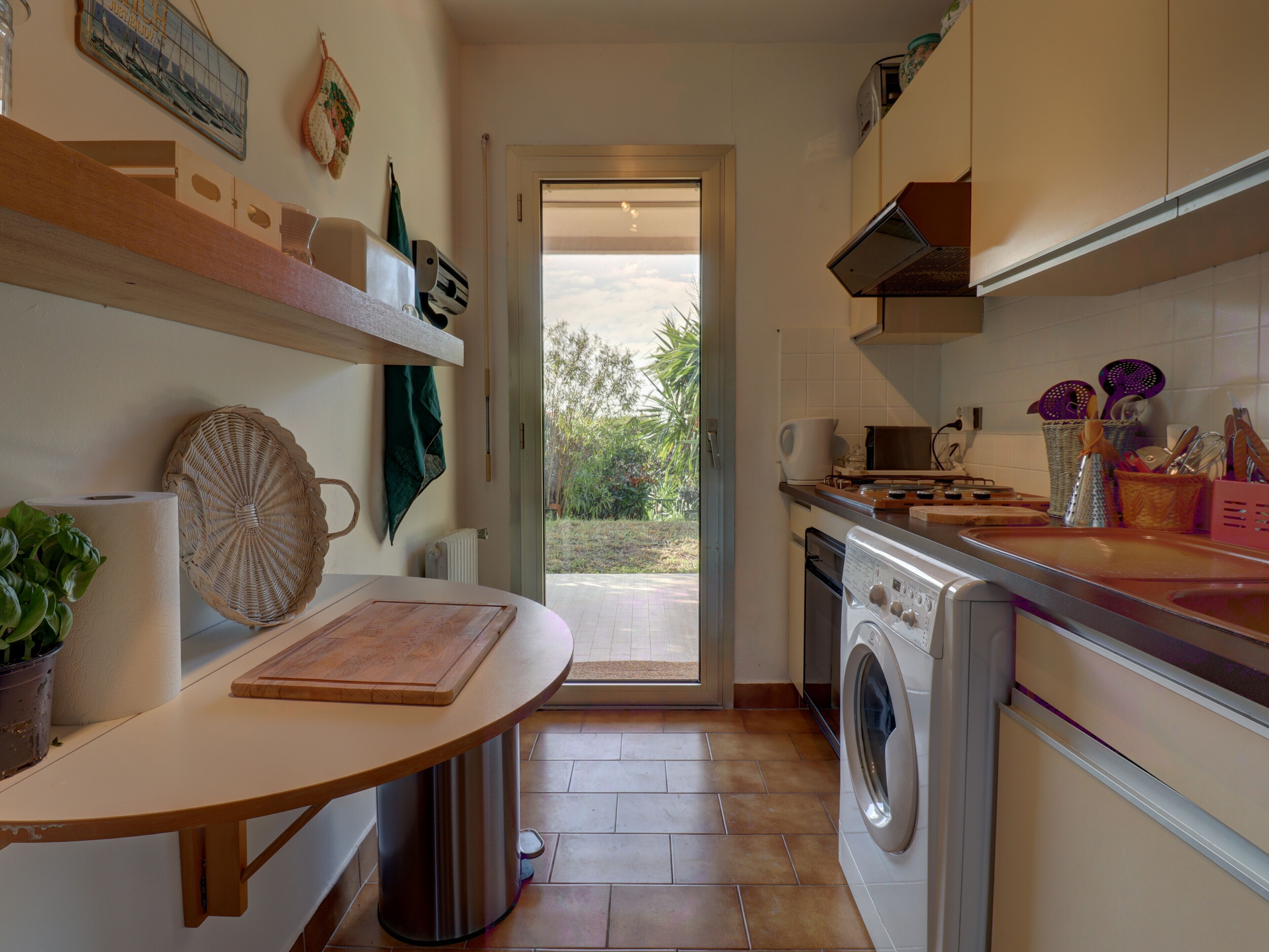 A kitchen with a built-in oven, microwave, and washing machine. There is a window providing a view of the outdoors.