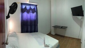 A small, simple room with a bed, a wall-mounted TV, a small table, and a ceiling fan. - Arrecifes 2 (Cartagena de Indias)