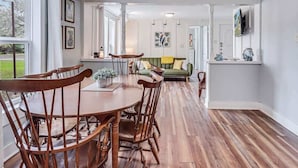 Un coin repas avec des chaises et une table en bois, un canapé vert et un espace cuisine équipé d’un téléviseur.