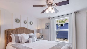 Une chambre avec un grand lit, un ventilateur de plafond, une fenêtre avec des rideaux et une vue sur l’extérieur.