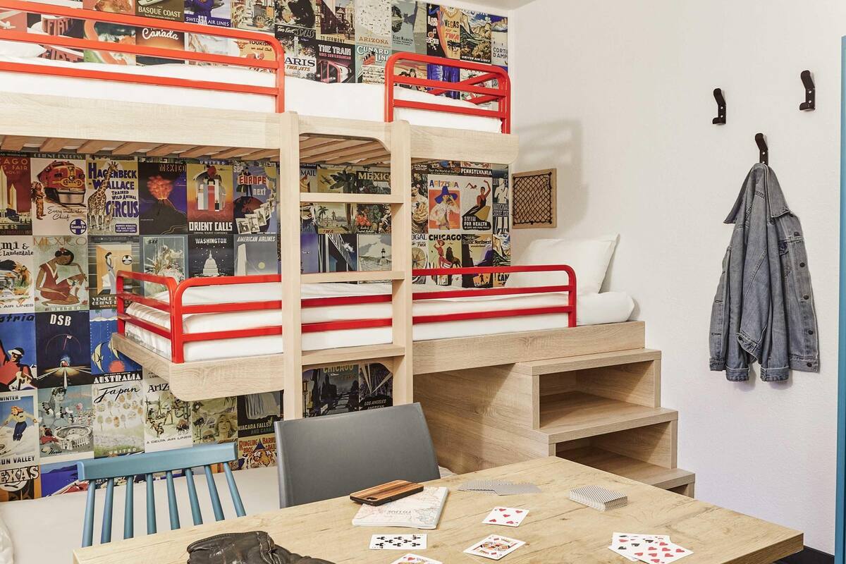 A bunk bed room with posters, a desk with playing cards, and a jacket hanging on the wall.