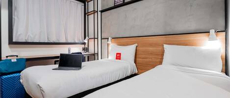 A hotel room with two beds, a desk, a laptop, a suitcase, and a window with curtains.