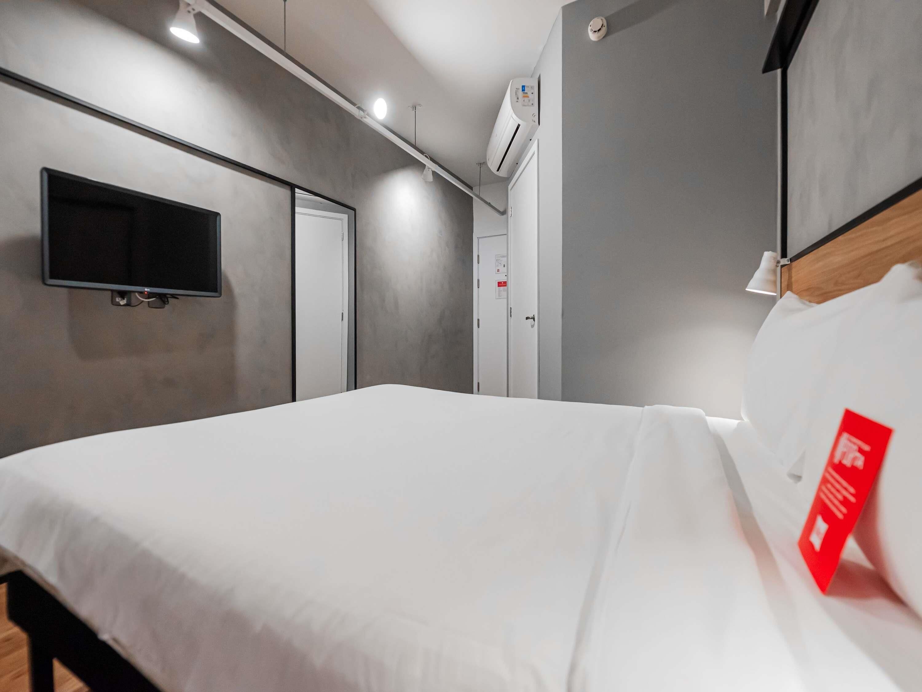 Una habitación de hotel moderna con una cama grande, un televisor de pantalla plana montado en la pared y un equipo de aire acondicionado instalado en el techo.