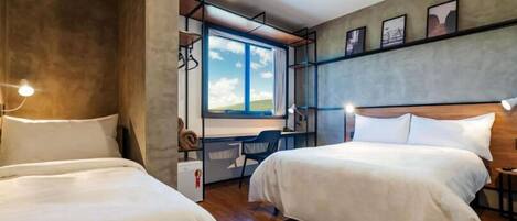 A room with two beds, a desk, a chair, and a window with a view of the sky.