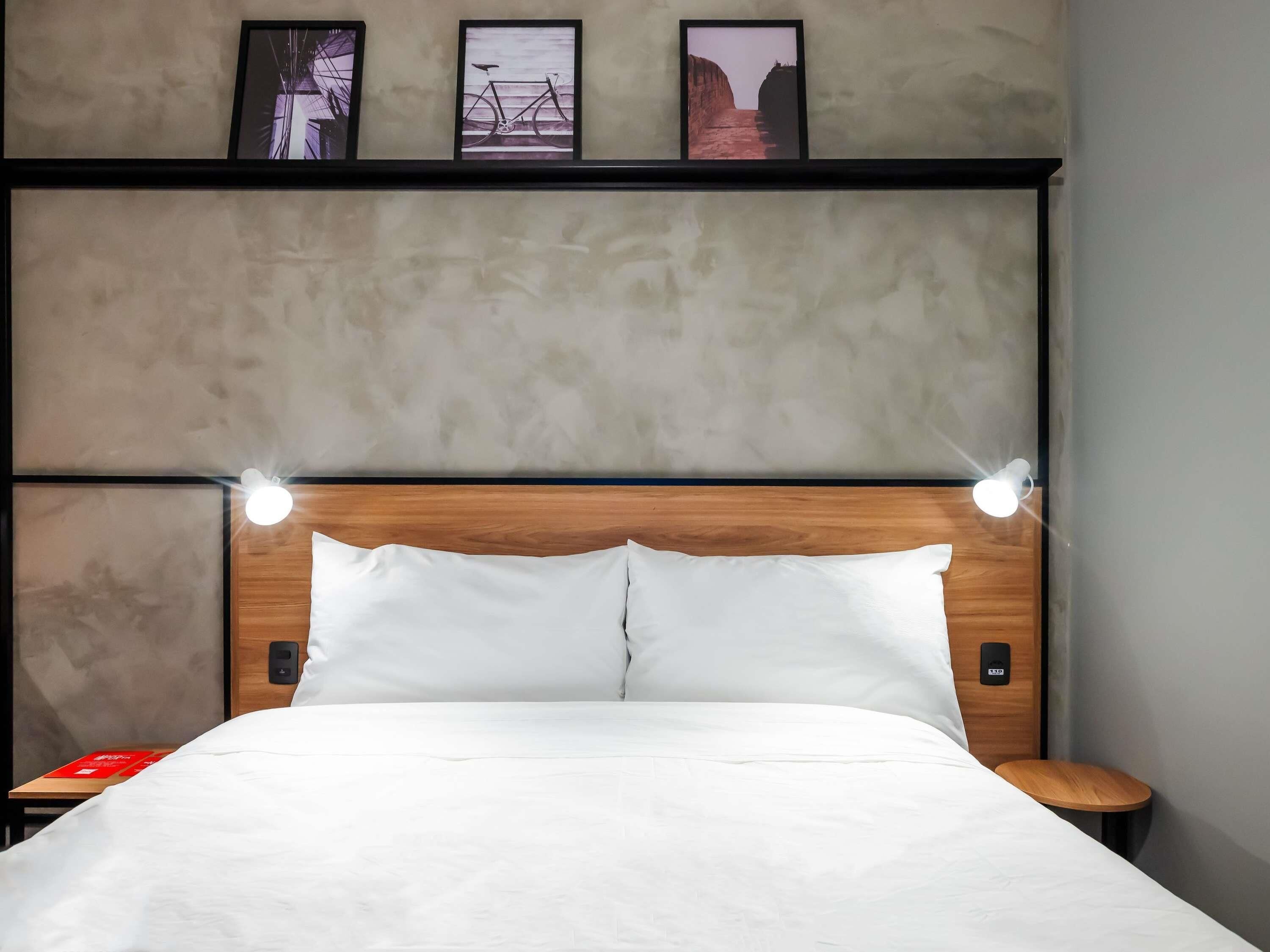 Une chambre d’hôtel comprenant un lit, des tables de chevet, une tête de lit dotée d’un éclairage intégré et des tableaux encadrés accrochés au mur.