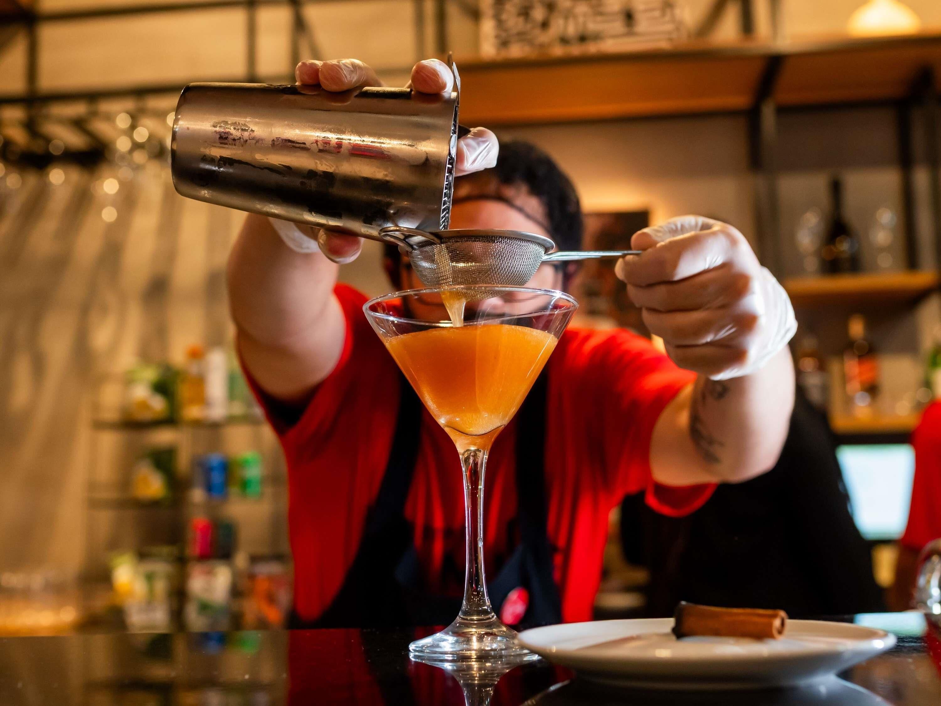 A person pouring a drink into a martini glass.