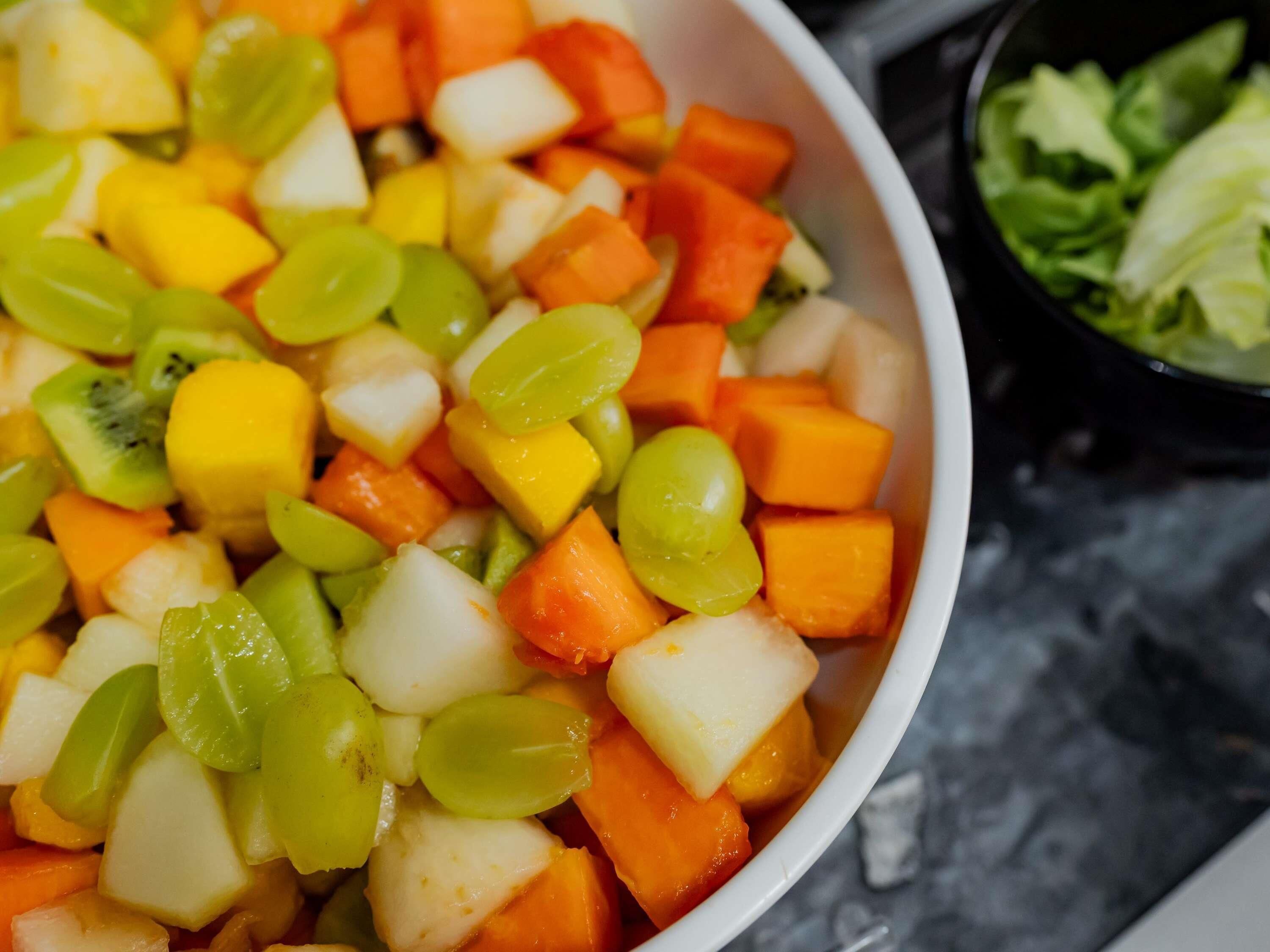 Una ciotola di macedonia con kiwi, mango e uva ben visibili.