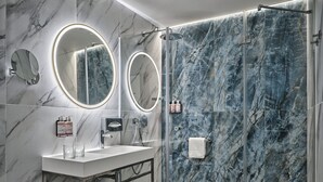 Un baño moderno con paredes de mármol, cabina de ducha de vidrio y dos espejos sobre lavamanos.