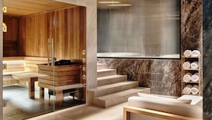 A modern spa area with wooden paneling, a glass-enclosed sauna, marble steps, and a wooden shelf with towels. - Mövenpick Grand Hotel Wroclaw (Wroclaw)