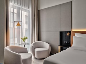 A hotel room with a bed, two armchairs, a small table, a floor lamp, and a fireplace. - Mövenpick Grand Hotel Wroclaw (Wroclaw)