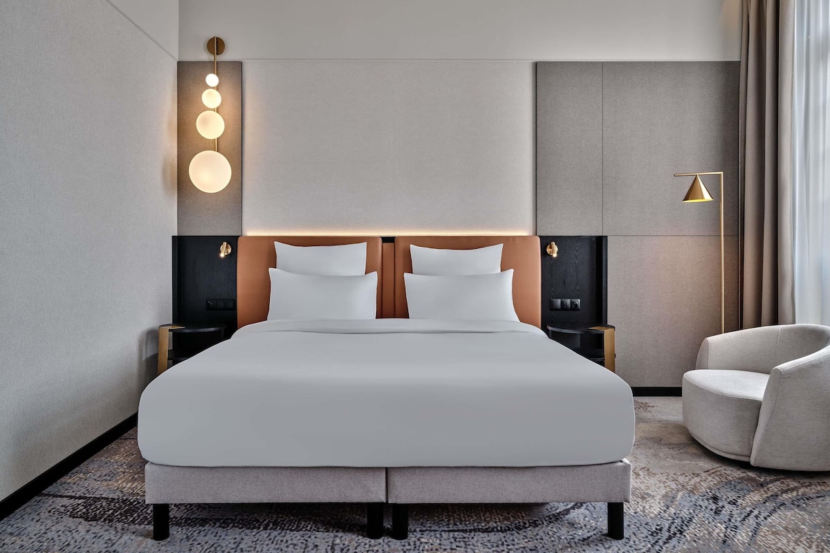 Ein modernes Hotelzimmer mit einem großen Bett, einem Nachttisch, einer Wandlampe und einem Sessel.