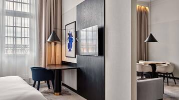 Ein Hotelzimmer mit einem Bett, einem Schreibtisch mit Stuhl, einem kleinen Tisch, zwei Pendelleuchten und einem großen gerahmten Bild an der Wand.