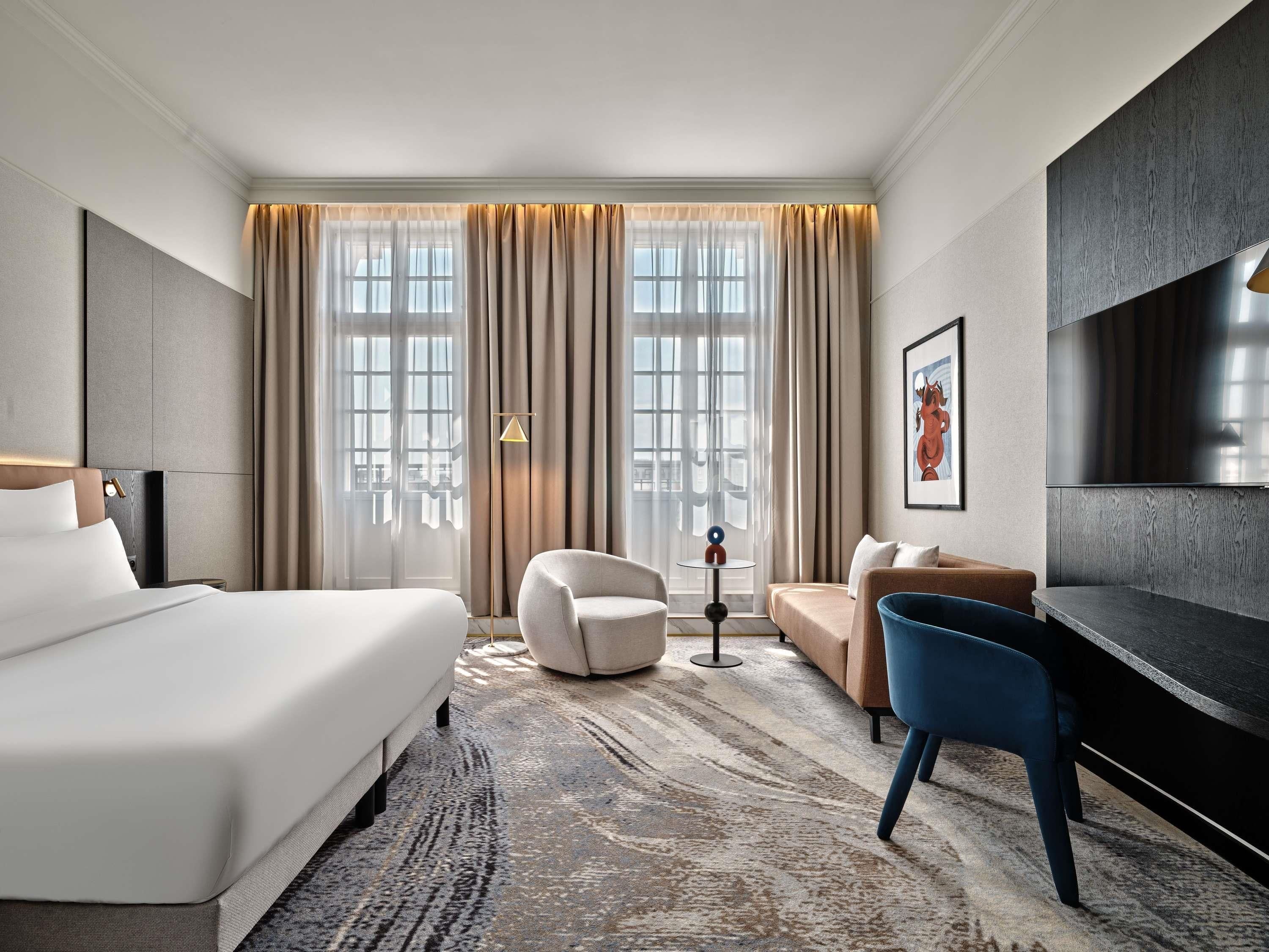 Une chambre d’hôtel avec un grand lit, un canapé, un fauteuil, une télévision et une lampe sur pied.