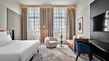 Une chambre d’hôtel avec un grand lit, un canapé, un fauteuil, une télévision et une lampe sur pied.