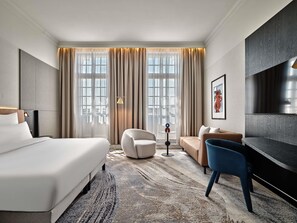 A hotel room with a large bed, a sofa, a chair, a TV, and a floor lamp. - Mövenpick Grand Hotel Wroclaw (Wroclaw)