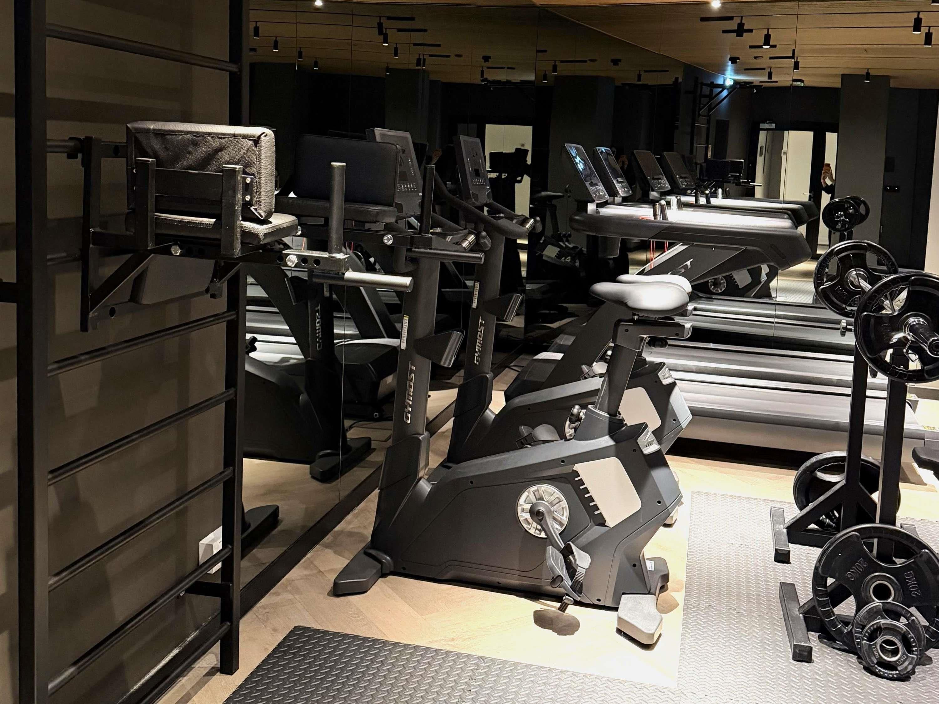 Ein Fitnessstudio mit verschiedenen Trainingsgeräten, darunter Laufbänder, Kraftgeräte und Kurzhanteln.