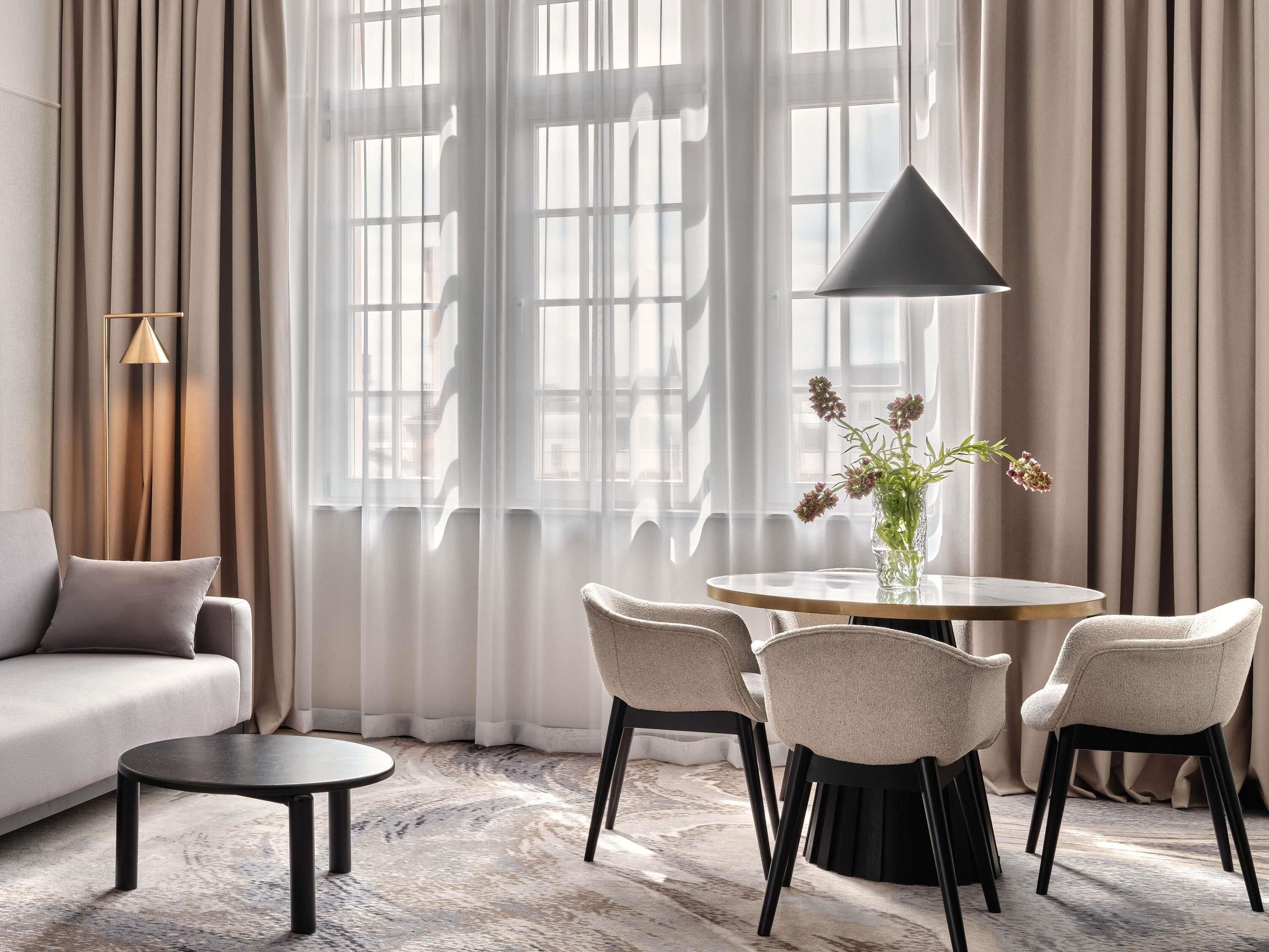 Un salon moderne avec un canapé, une table ronde entourée de chaises, un vase de fleurs et une lampe.