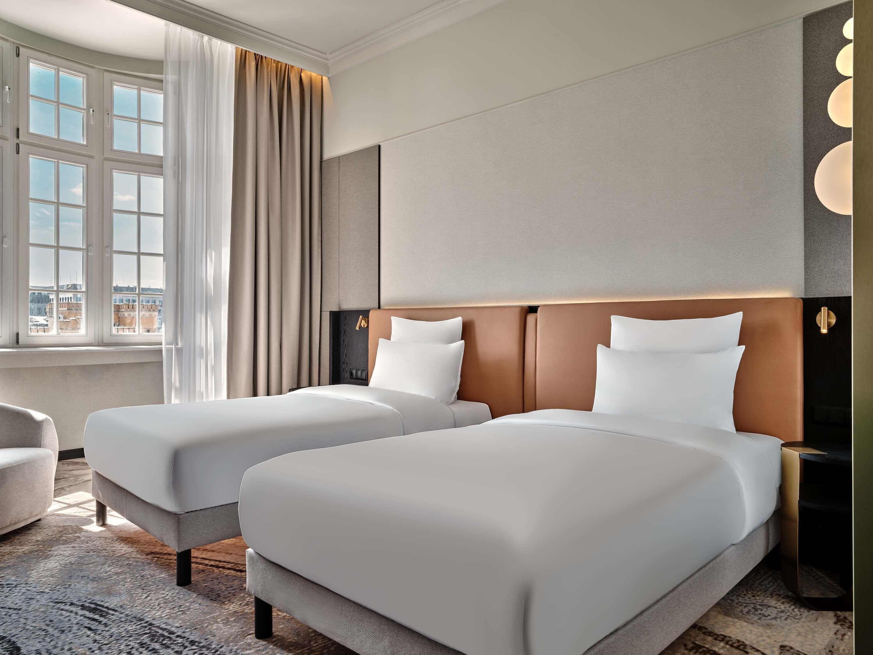 Une chambre d’hôtel avec deux lits, une fenêtre avec des rideaux, un canapé et une table de chevet.