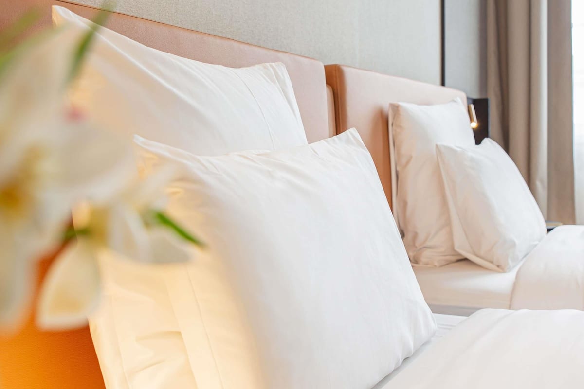 Ein Hotelzimmer mit einem ordentlich bezogenen Bett, weißer Bettwäsche und einem Kopfteil.