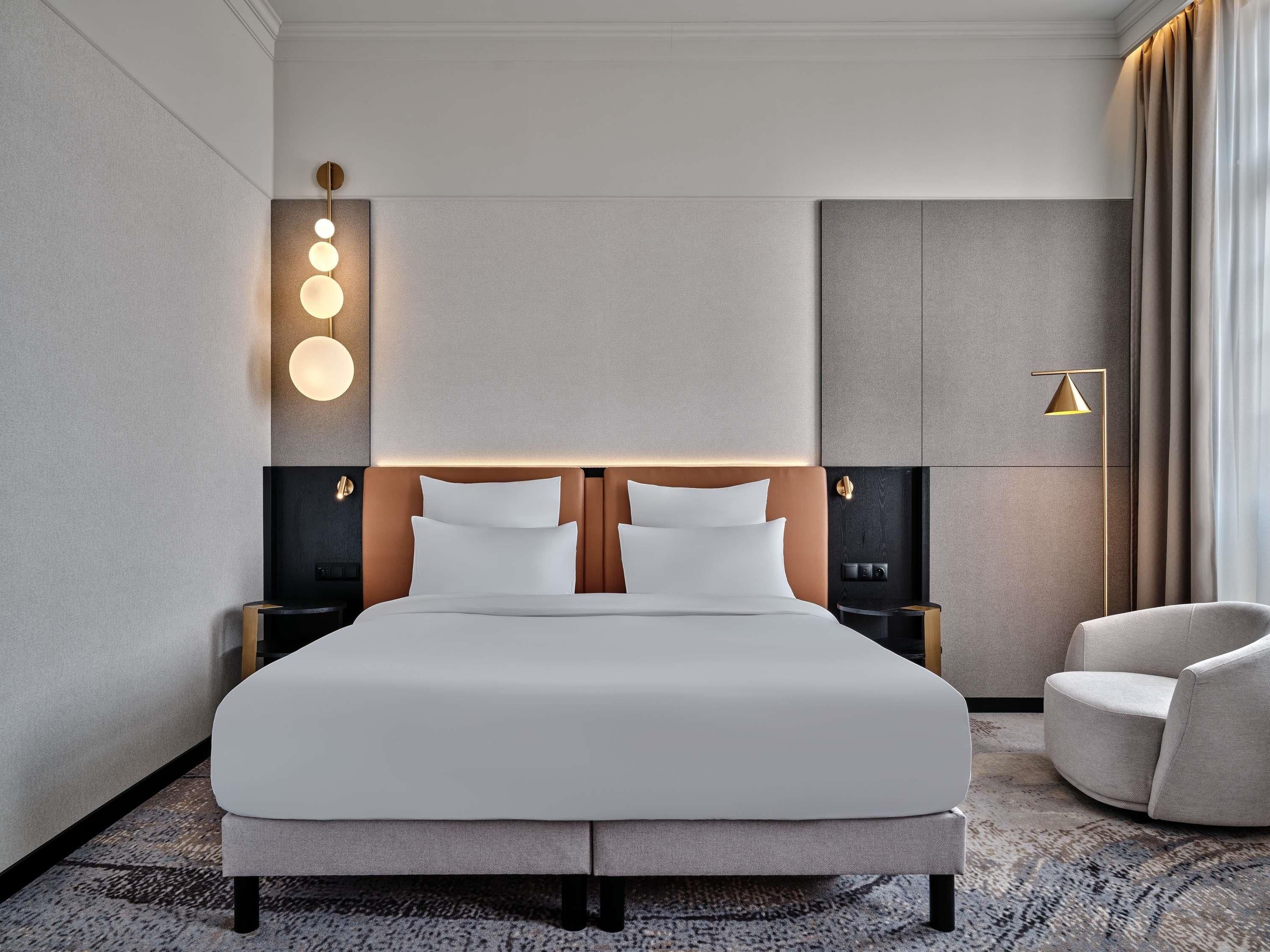Une chambre d’hôtel moderne avec un grand lit, une table de chevet, une lampe fixée au mur et une chaise.