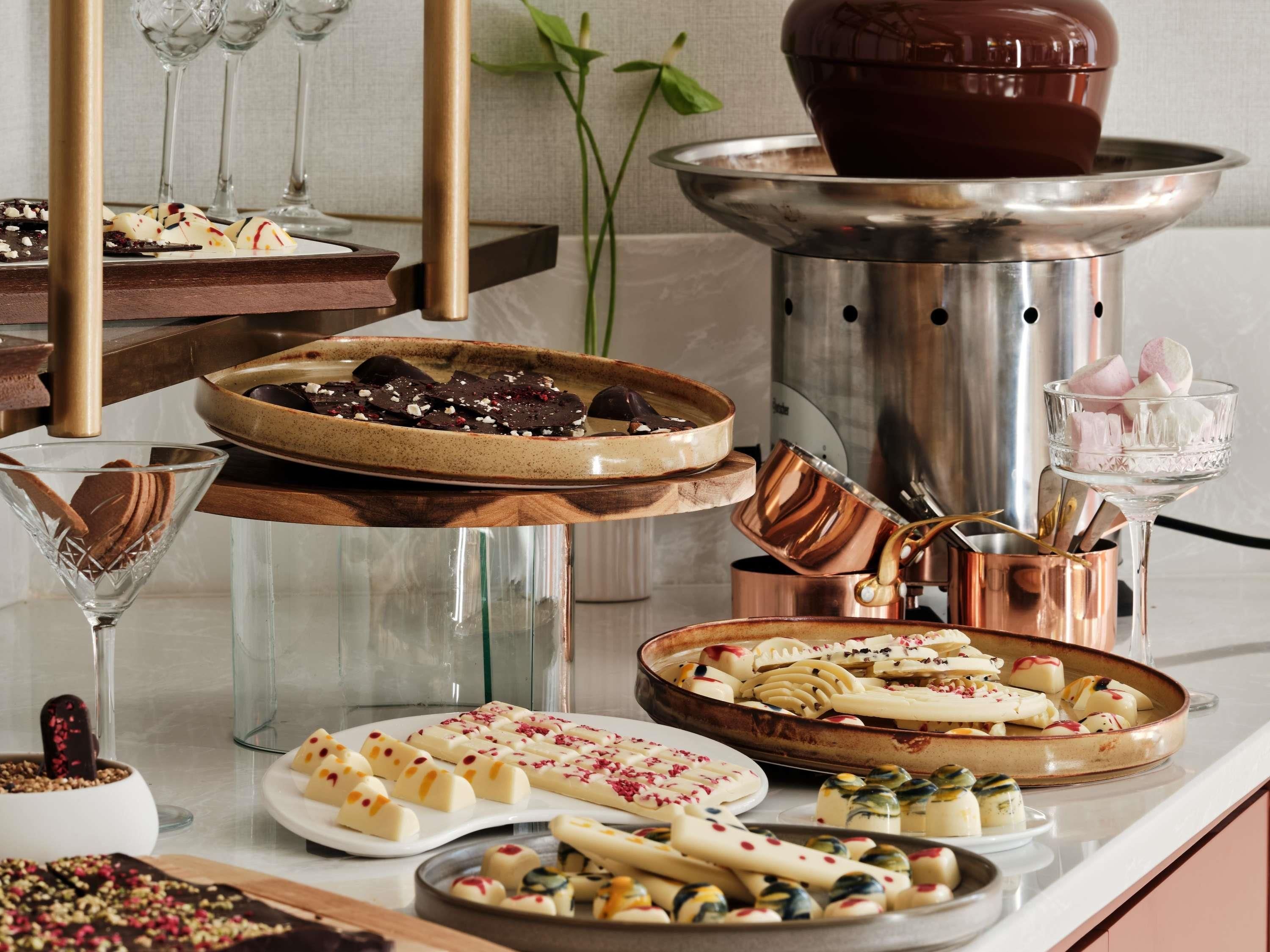 Une variété de desserts est disposée sur une table, notamment des gourmandises enrobées de chocolat et des confiseries blanches décorées de rouge et de jaune.