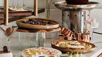 Une variété de desserts est disposée sur une table, notamment des gourmandises enrobées de chocolat et des confiseries blanches décorées de rouge et de jaune.
