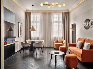 A modern living room with a sofa, ottoman, and a dining area with chairs and a table. - Mövenpick Grand Hotel Wroclaw (Wroclaw)