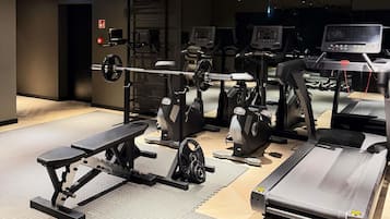 Un gimnasio con máquinas de cardio, equipo de levantamiento de pesas y una banca.