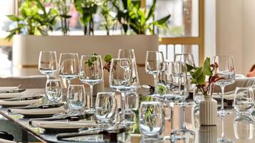 A dining table set with multiple wine glasses and plates, surrounded by potted plants.