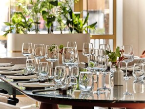 A dining table set with multiple wine glasses and plates, surrounded by potted plants.