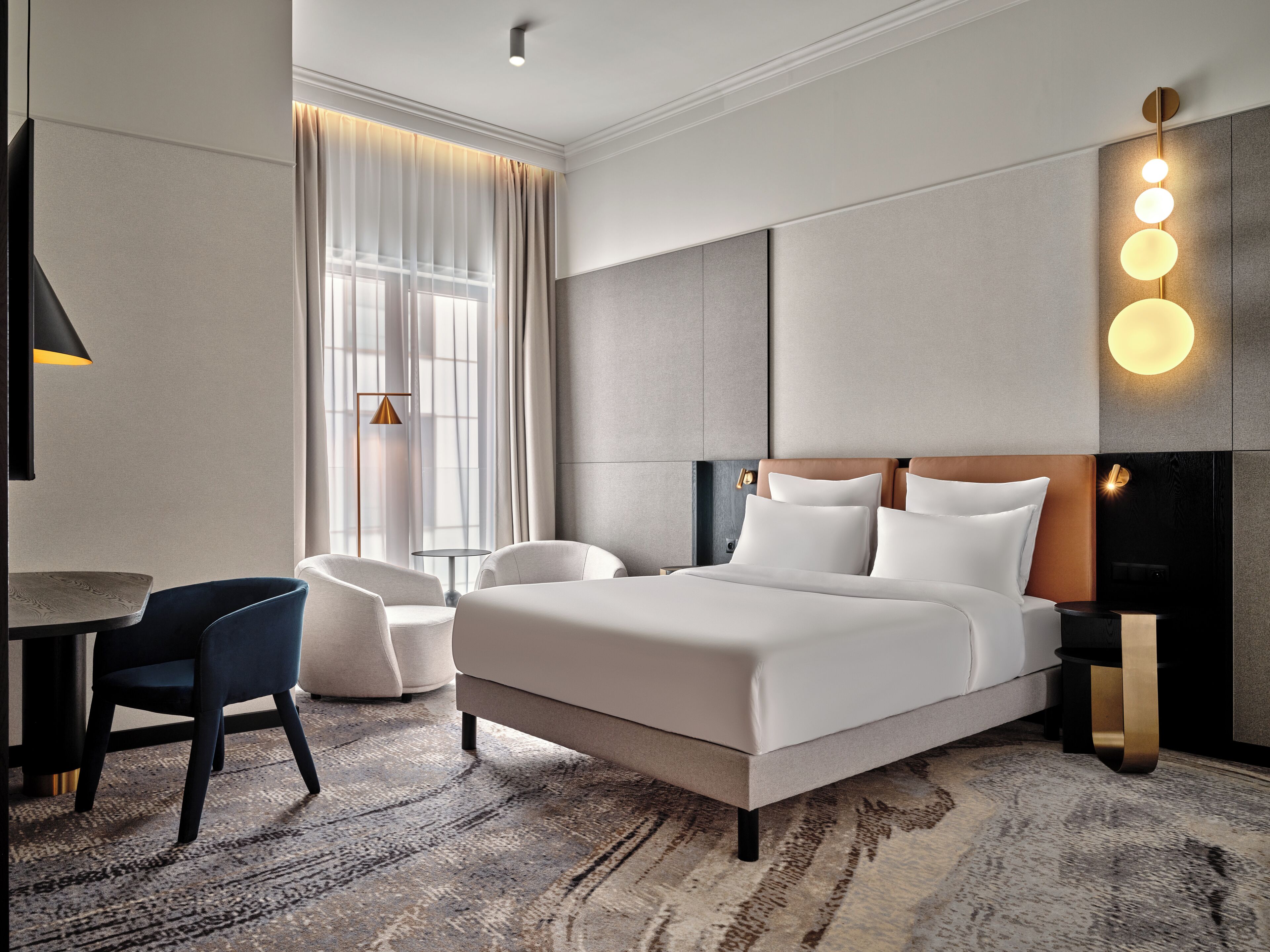A modern hotel room with a large bed, a desk, a chair, and a sofa.
