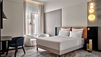 A modern hotel room with a large bed, a desk, a chair, and a sofa.