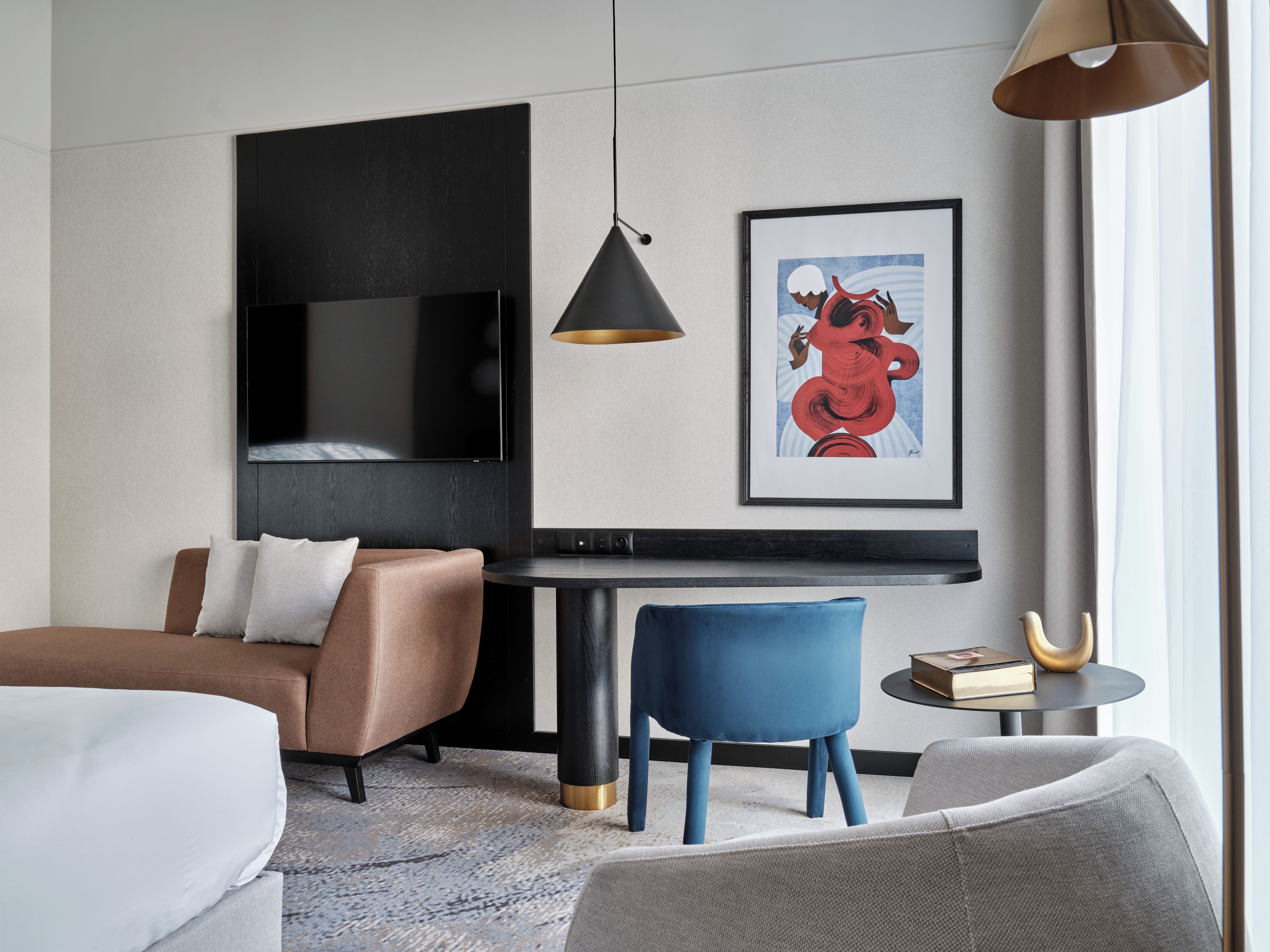Una habitación de hotel moderna con una televisión de pantalla plana, una obra de arte enmarcada, una mesa redonda y un sofá.