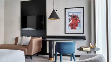 Una habitación de hotel moderna con una televisión de pantalla plana, una obra de arte enmarcada, una mesa redonda y un sofá.