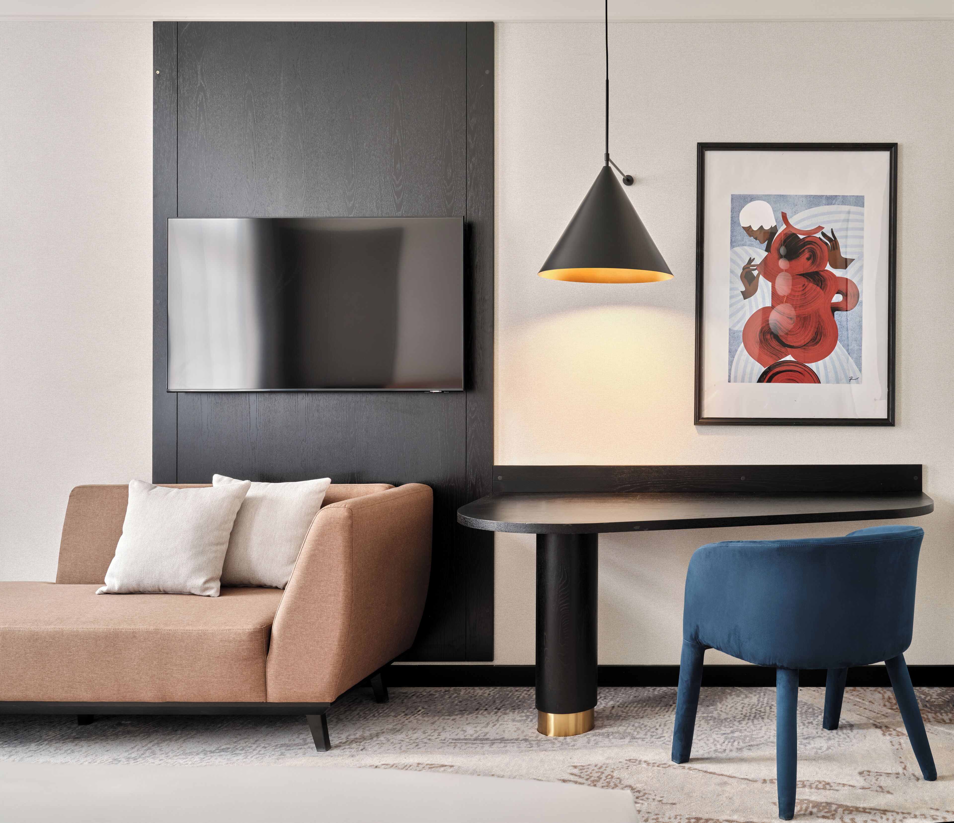 A modern living room with a sofa, a blue chair, a table, a mounted TV, a pendant light, and a framed artwork.